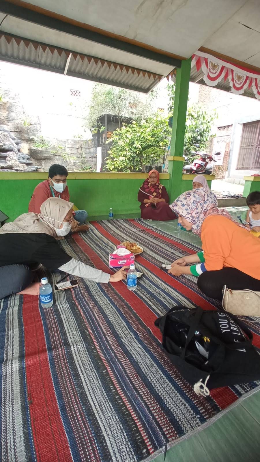A home visit with Mapan group leaders during the pandemic, sitting together on woven mats with phones out