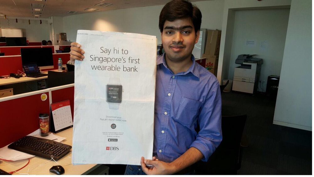Holding the Straits Times full-page ad, Singapore's first wearable bank, DBS PayLah